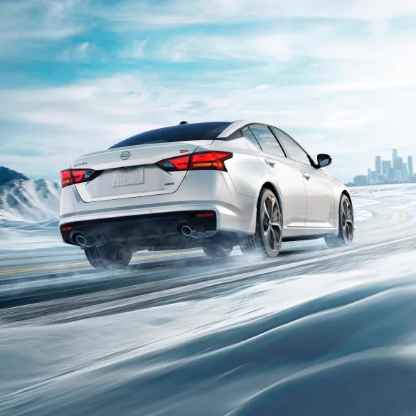 2027 Nissan Altima in white seen from behind driving in snowy landscape illustrating all-wheel drive at HGreg Nissan Kendall in Palmetto Bay FL