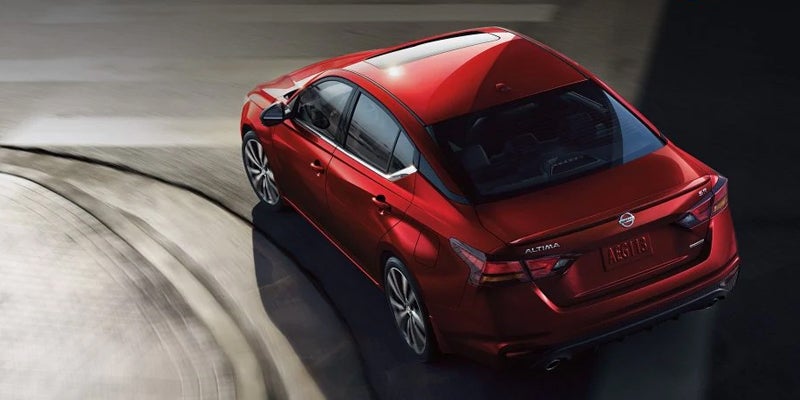 Red Nissan Altima sedan driving on a curved road