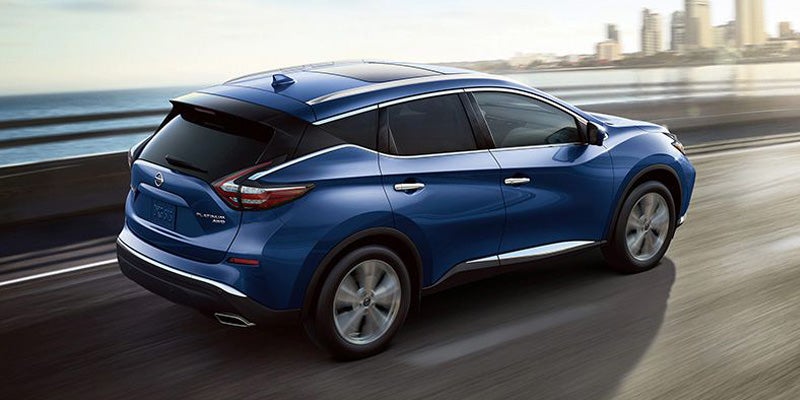 Rear-angle view of a blue Nissan Murano Platinum AWD driving quickly on a highway next to the ocean.