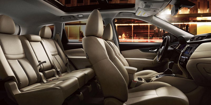 View of a spacious car interior featuring tan leather seats, dark dashboard, and open sunroof