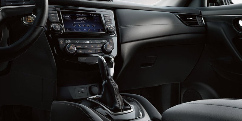 The dark gray interior of a car shows the dashboard, steering wheel, infotainment screen, and gear shift