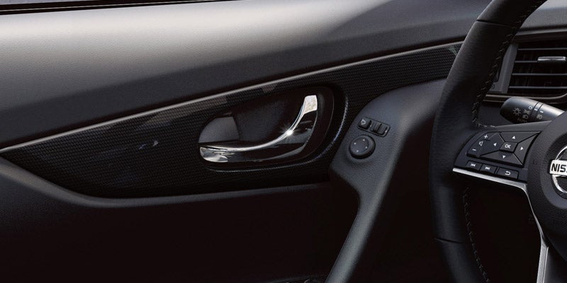Car interior showing the chrome door handle, carbon fiber trim, mirror controls