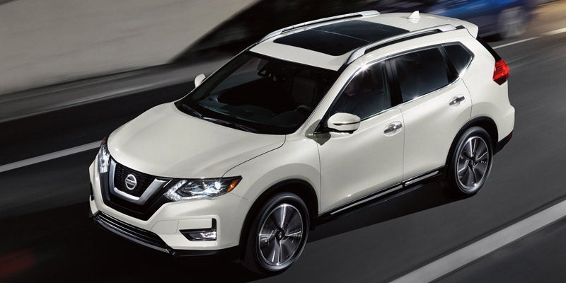 A white Nissan Rogue SUV with a sunroof, seen from above, driving on a highway at speed