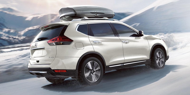 White SUV with a rooftop cargo box moving left through a snowy mountainous landscape