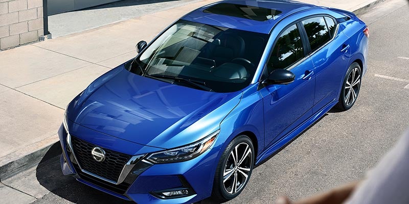 Top-down view of a shiny blue Nissan Sentra parked on a curb beside a gray building.