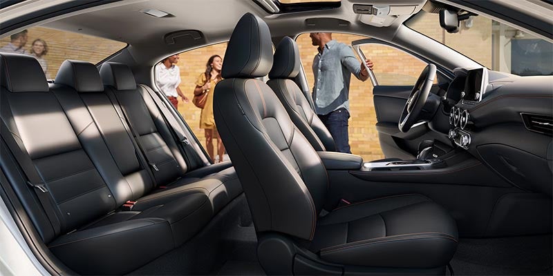 Interior view of a car with dark leather seats, and blurred people standing outside the open doors