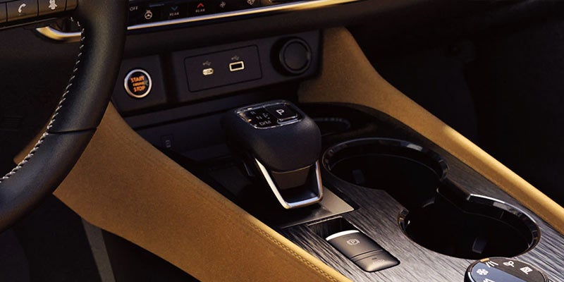 The beige and dark interior of a car, showing the gear shift, cup holders, and start engine button