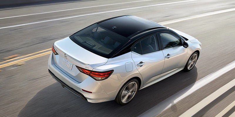 Overhead view of a silver sedan with a black roof and tinted windows, driving on a highway with blurred lines