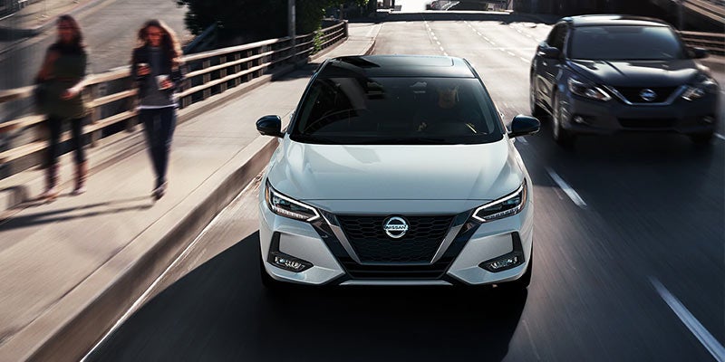 A white Nissan Sentra drives forward on a multilane road.