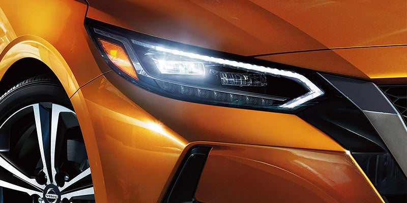 Close-up of a vibrant orange car's illuminated headlight