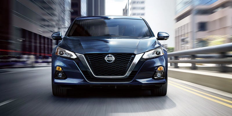 Front view of a dark blue Nissan Altima driving on a blurred, motion-streaked city street