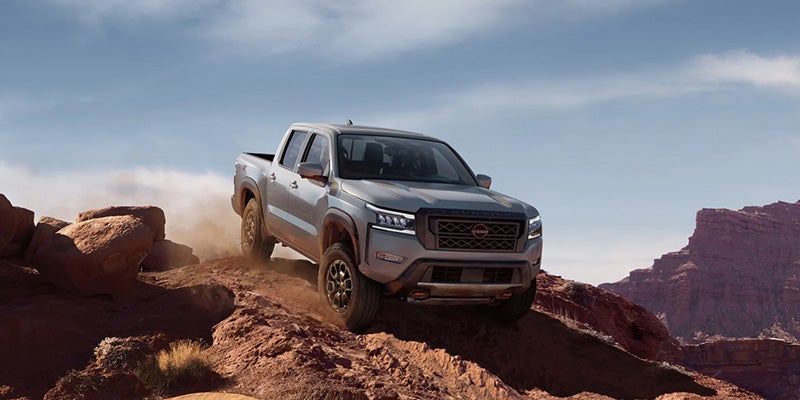 Gray Nissan Frontier PRO-4X truck drives up a dusty, rocky desert hill