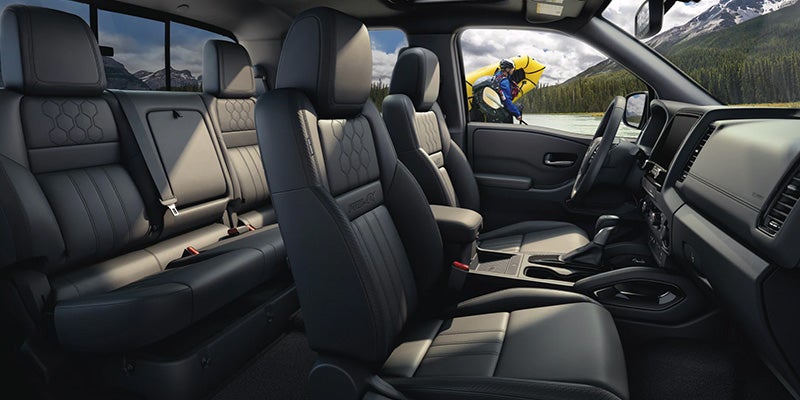 View from inside a car: dark gray leather seats, passenger door open to reveal a person with a yellow kayak on a lake.