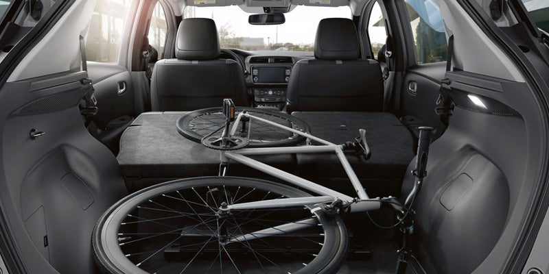 A white road bicycle with the front wheel removed, stored in the back of a car