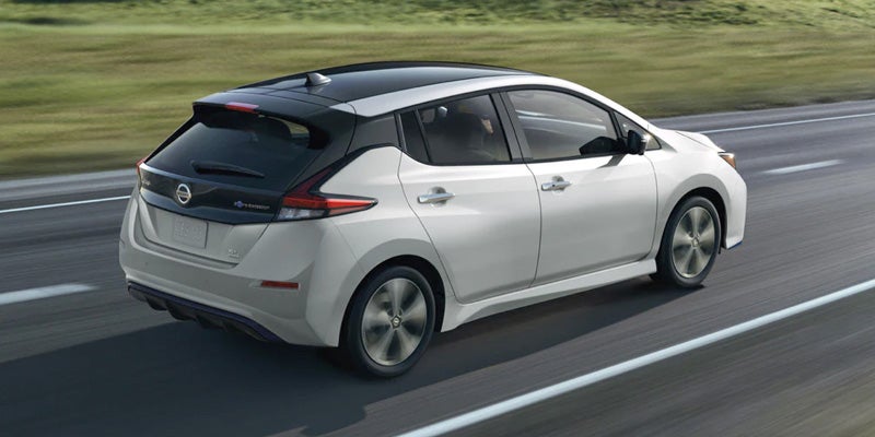 Rear-view of a two-tone white and black Nissan Leaf driving on a multi-lane highway on a sunny day.