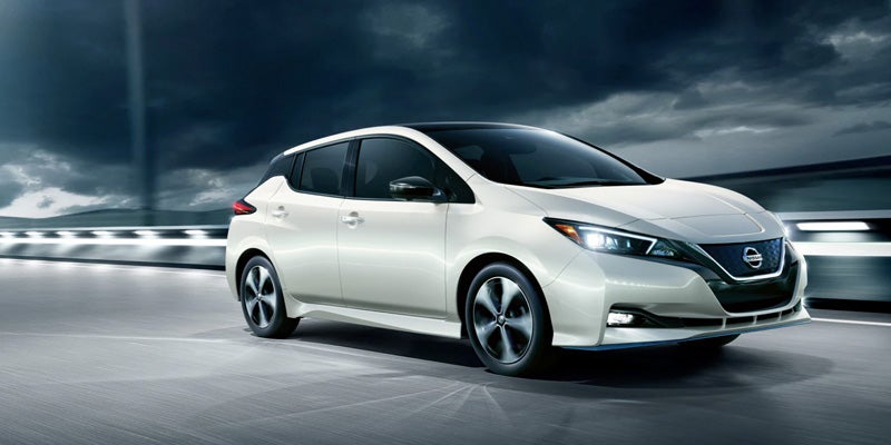 A white Nissan LEAF car is driving on a highway under a stormy, clouded sky