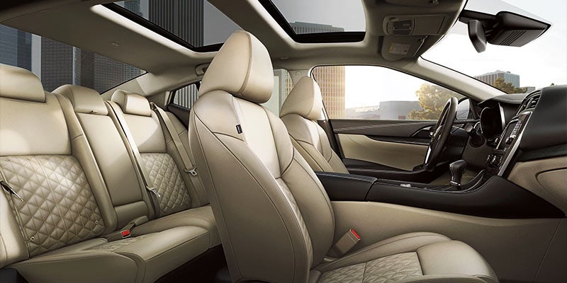 Interior view of a car with light tan perforated leather seats, black dashboard, sunroof, and city visible outside