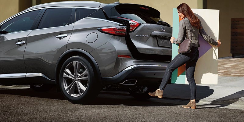A woman is using a foot motion to open the back hatch of a gray Nissan Murano SUV