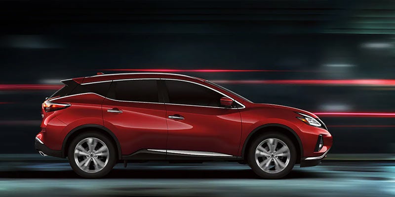 Side view of a red Nissan Murano crossover speeding past with blurred light streaks behind it