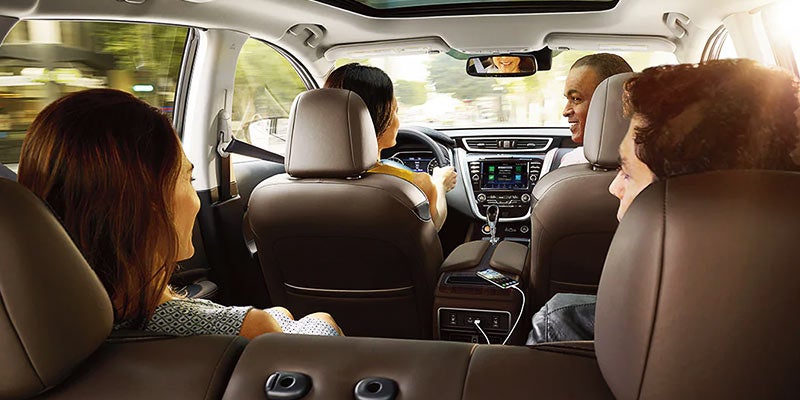 View from rear car seat of four adults riding in a car, with the driver seen from behind,