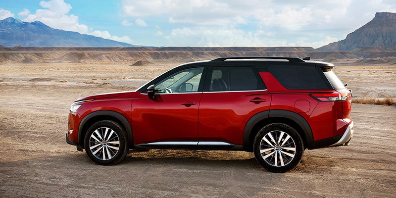 A red mid-size SUV with black roof and wheel wells parked on a dirt road in a desert landscape