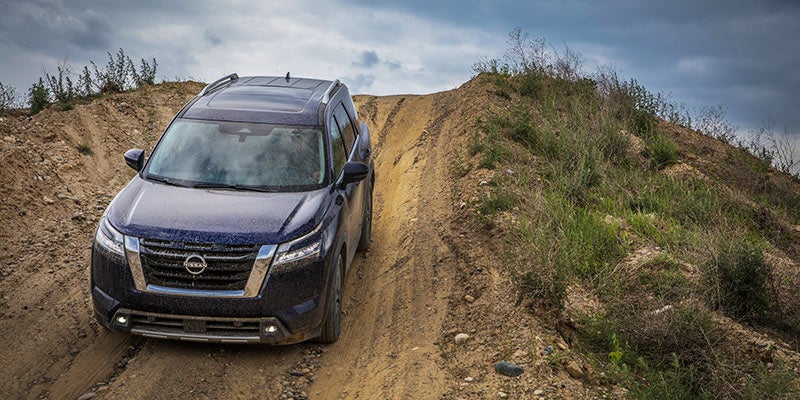 A dark blue SUV driving down a steep dirt road on a hillside