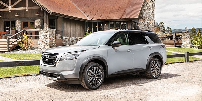 Light grey SUV with a black roof parked on a gravel driveway in front of a rustic lodge