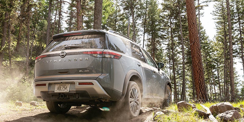 Rear view of a grey Nissan Pathfinder driving on an unpaved, dusty forest road