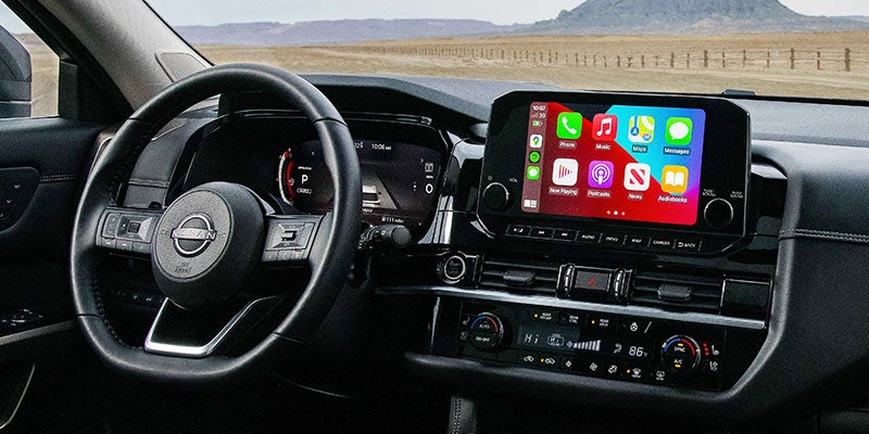 Driver's view of a black Nissan car interior with a large touchscreen displaying apps and a digital dashboard