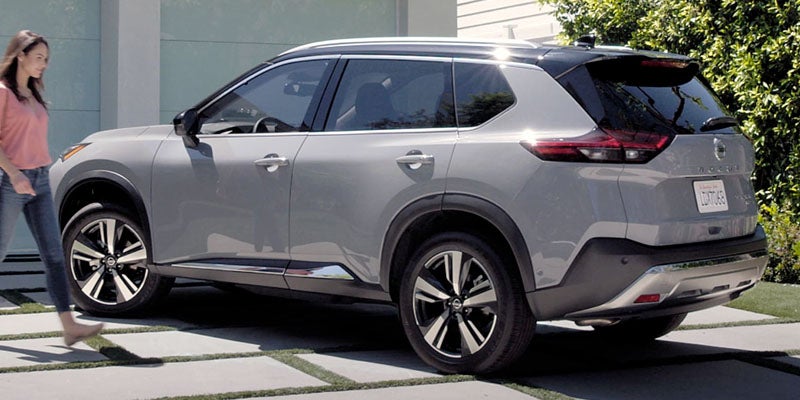 Right profile of a light grey SUV with a black roof and woman walking beside it on a patterned driveway