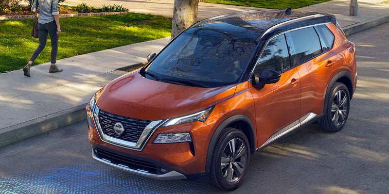 Orange Nissan Rogue SUV with a black roof parked on the street with a person walking on the sidewalk