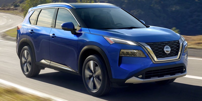 A blue Nissan Rogue SUV with silver trim driving on a winding paved road