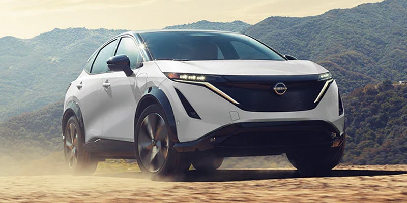 White Nissan Ariya EV SUV driving on a dirt road, kicked-up dust visible