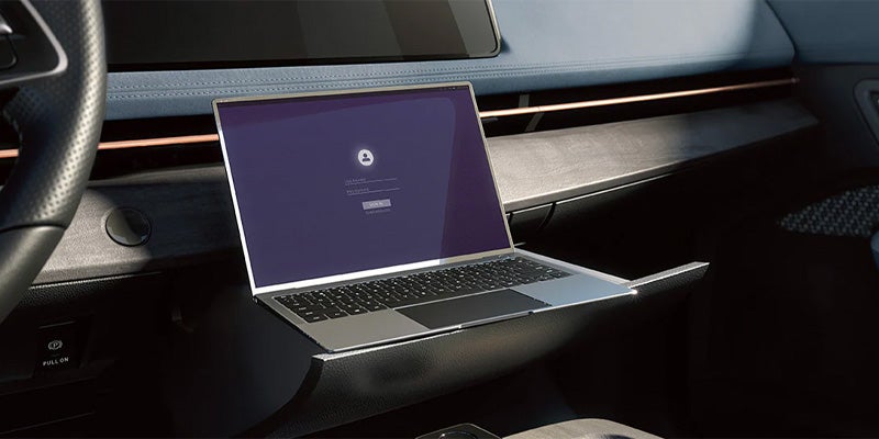 A laptop with a login screen on a pull-out tray in a car's dashboard.