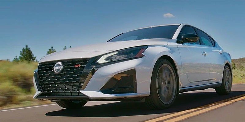 Front and side view of a white Nissan Altima SR sedan driving on a highway.