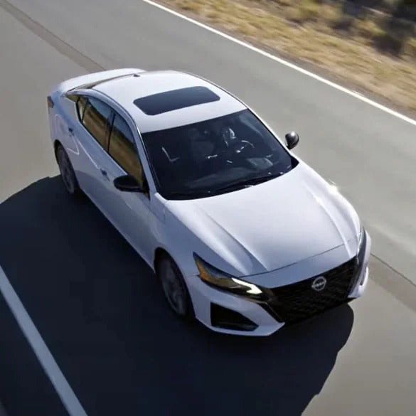 Overhead view of a white sedan with a black sunroof driving on a paved road with a white line.