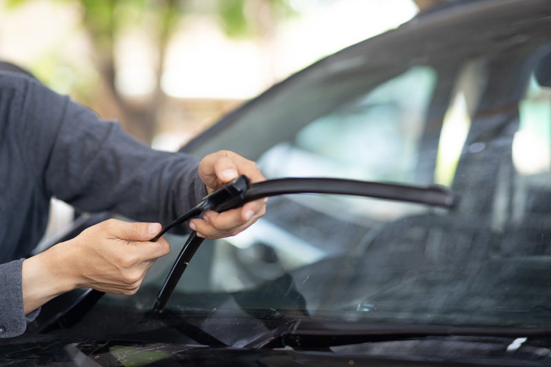 A person's hands replacing a worn windshield wiper on a car.